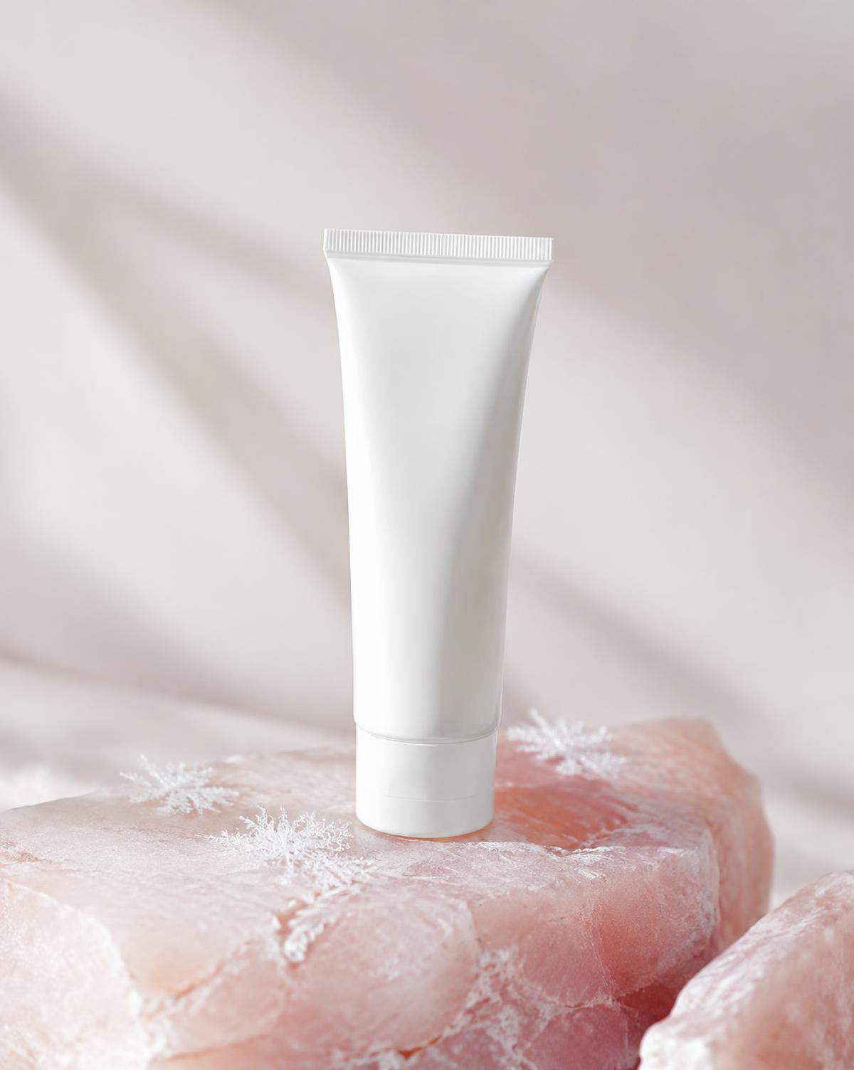 White sunscreen tube on pink stone with frost crystals